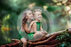 Children a boy and a girl in the forest near a fabulous green lake sitting on a fallen tree