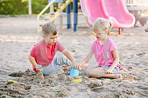 Children boy and girl friends preschoolers playing with sand and toys in sandbox on summer day