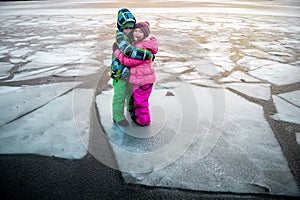 Children boy and girl hug each other staying on ice block in river. Little traveler kid in bright winter clothes walking