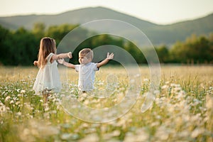 Children a boy and a girl hug and kiss each other amicably in a flowering field against the backdrop of hilly mountains.