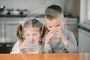 Children boy and girl in the kitchen drinking water from glasses