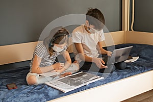 Children boy and a girl in a medical mask carry out lessons through laptop. Online education during a pandemic epidemic.