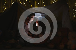 Children boy and girl playing and frighten each other with flashlight in tent at night