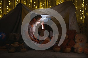 Children boy and girl playing and frighten each other with flashlight in tent at night