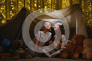 Children boy and girl playing and frighten each other with flashlight in tent at night