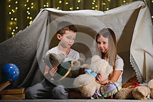 Children boy and girl playing and frighten each other with flashlight in tent at night