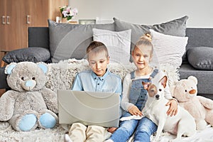 Children boy and girl playing on tabletand watching videos on laptop. Home schooler kids with dog, home schooling, home education