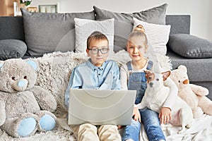 Children boy and girl playing on tabletand watching videos on laptop. Home schooler kids with dog, home schooling, home education