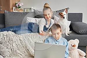 Children boy and girl playing on tabletand watching videos on laptop. Home schooler kids with dog, home schooling, home education