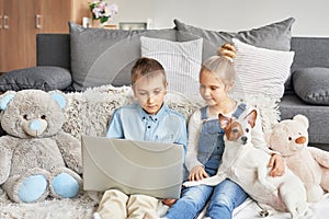 Children boy and girl playing on tabletand watching videos on laptop. Home schooler kids with dog, home schooling, home education