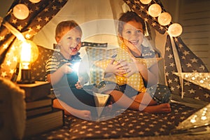 Children boy and girl reading book with flashlight in tent