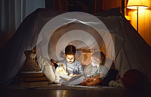 Children boy and girl reading book with flashlight in tent