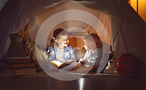 Children boy and girl reading book with flashlight in tent