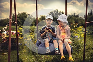 Children boy and girl swinging together in summer day on backyard in countryside concept happy chilhood