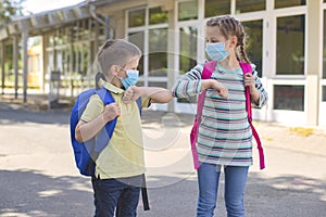 Children, a boy and a girl, wearing masks, greet their elbows on the street in the schoolyard due to the coronavirus epidemic.