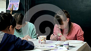 Children boys and girls sitting together around the table in classroom and drawing. With them is their young and