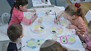 Children boys and girls sitting together around the table in classroom and drawing. With them is their young and