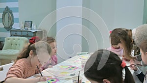 Children boys and girls sitting together around the table in classroom and drawing. With them is their young and