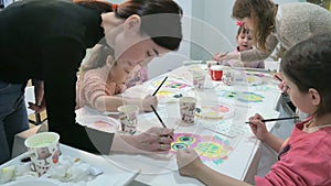 Children boys and girls sitting together around the table in classroom and drawing. With them is their young and