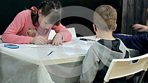 Children boys and girls sitting together around the table in classroom and drawing. With them is their young and