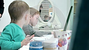 Children boys sitting together around the table in classroom and drawing. With them is their young and beautiful teacher