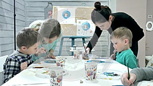 Children boys sitting together around the table in classroom and drawing. With them is their young and beautiful teacher