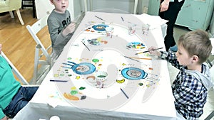 Children boys sitting together around the table in classroom and drawing. With them is their young and beautiful teacher