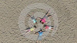 Children in bright clothes lie on the sand in the shape of a star