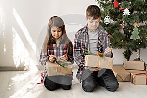 Children brother and sister with Christmas gifts are sitting on the floor of the room near the tree. Boy and girl look