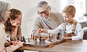 Children brother and sister playing chess while sitting in living room with senior grandparents