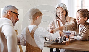 Children brother and sister playing chess while sitting in living room with senior grandparents