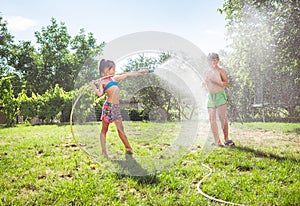 Children brother and sister, playing with watering hose in hot summer afternoon