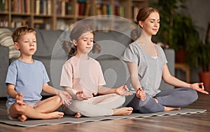 Children brother and sister sitting in lotus pose on floor and meditating with closed eyes with mom