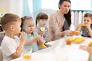 Children and carer together eat fruit as a snack in the kindergarten, daycare or school