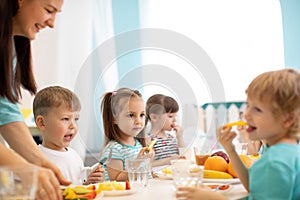 Children and carer together eat fruits and vegetables in kindergarten or daycare