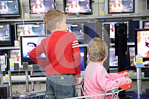 Children in carriage for purchases look at TVs in