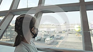 Children caucasian at airport with wearing protective medical mask on head against the background of plane. Coronavirus