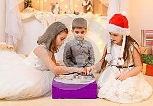 Children celebrating christmas or new year, drink tea, eat cookies and play with the toy dishes in home interior decorated with