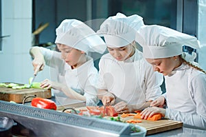 Children in chef`s hat grind vegetables on the kitchen.