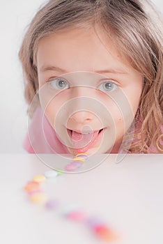 Children and chocolate. Joyful girl with sweets.A cheerful girl plays and eats chocolate multi-colored round candies on a light