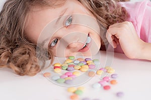 Children and chocolate. Joyful girl with sweets.A cheerful girl plays and eats chocolate multi-colored round candies on a light