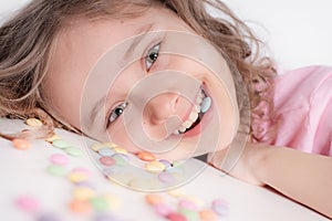 Children and chocolate. Joyful girl with sweets.A cheerful girl plays and eats chocolate multi-colored round candies on a light