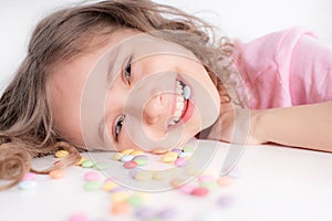 Children and chocolate. Joyful girl with sweets.A cheerful girl plays and eats chocolate multi-colored round candies on a light