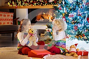 Children at Christmas tree and fireplace on Xmas eve. Family with kids celebrating Christmas at home. Boy and girl in matching