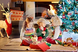 Children at Christmas tree and fireplace on Xmas eve. Family with kids celebrating Christmas at home. Boy and girl in matching