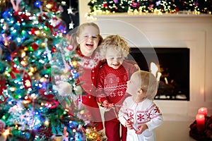 Children at Christmas tree. Kids at fireplace on Xmas eve