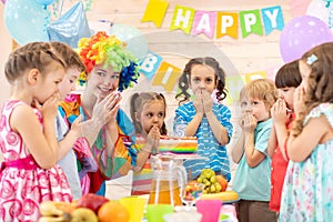 Children with clown celebrating birthday party. Kids stand arround festive table waiting surprise