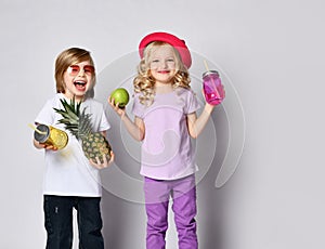 Children, colorful casual clothes. Laughing, holding yellow and pink cocktail bottles, apple, pineapple. Posing isolated on white