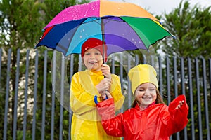 Children with a colorful rainbow umbrella, waterproof jacket and coat play in the rain.