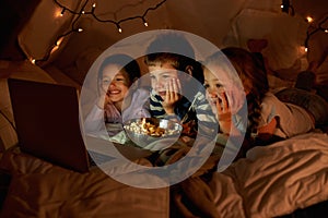 Children, computer and watch in tent at night with movies, film or cartoons for holiday adventure or vacation. Young boy